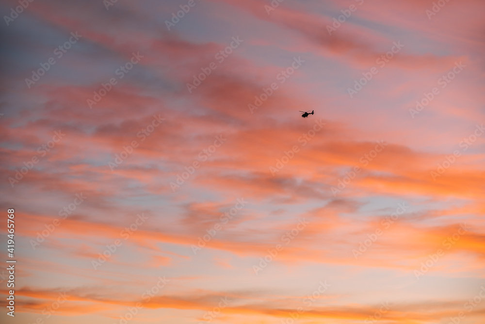 Remote view of helicopter silhouette on background of vivid sundown sky over city in evening Remote view of helicopter silhouette on background of vivid sundown sky over city in evening