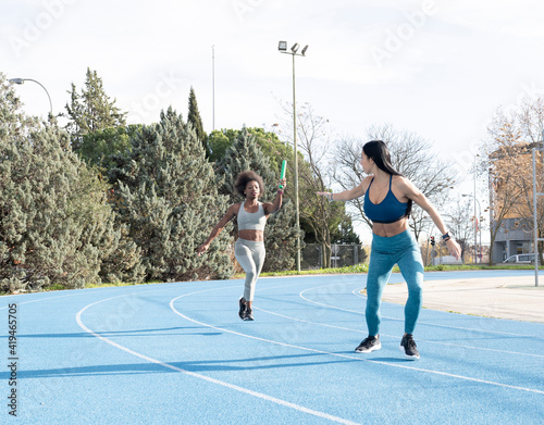 Fit multiracial female athletes passing baton while running along track at stadium during relay race photo