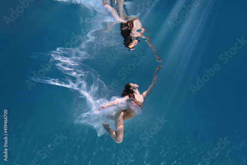 Fashionable and athletic girl free diver alone in the depths of the ocean. Swimmer brunette diving deep in ocean on blue underwater background. Pollution, plastic and ecology concept