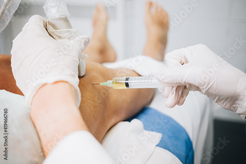 A doctor's hands pricking the knee with a needle while doing an ultrasound test on a patient stretched out on a hospital