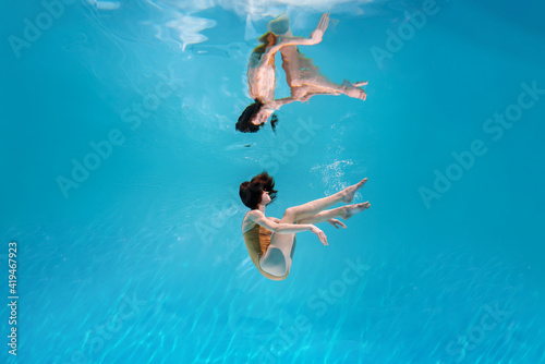 Fashionable and athletic girl free diver alone in the depths of the ocean. Swimmer brunette diving deep in ocean on blue underwater background. Concentration, freedom and beauty concept