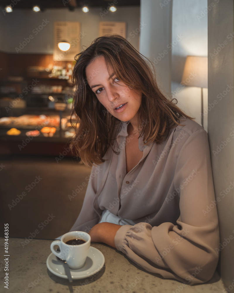 Confident young female in elegant blouse looking at camera while relaxing in cozy cafe with cup of coffee