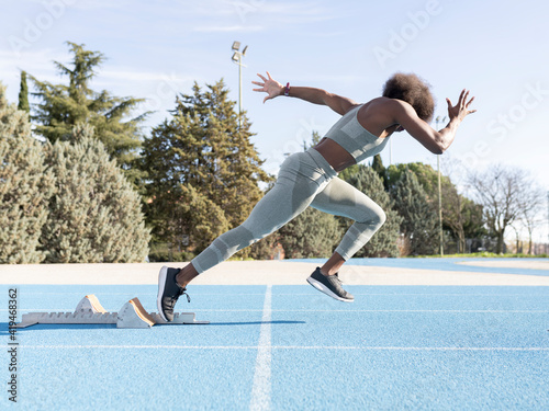 Side view of energetic African American female athlete running out of starting blocks during workout at stadium photo