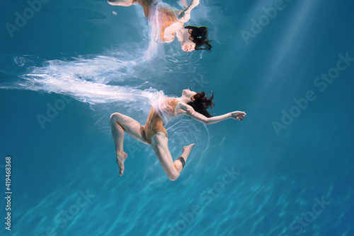 Fashionable and athletic girl free diver alone in the depths of the ocean. Swimmer brunette diving deep in ocean on blue underwater background. Pollution  plastic and ecology concept