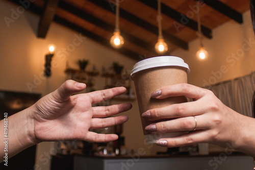 Detail shot of a woman's hands passing a cup of coffee to another woman who is about to grab it, in the cafeteria.