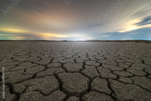 From above of drought cracked lifeless ground under colorful cloudy sky at sunset time