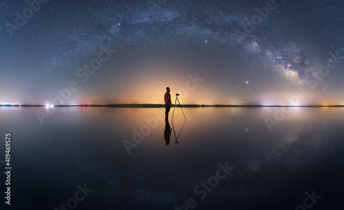Side view of anonymous photographer with photo camera standing under night sky with glowing stars in long exposure photo
