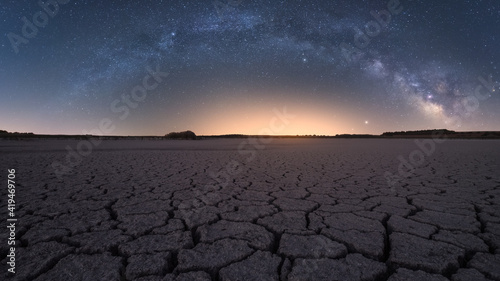 Picturesque panoramic view of cracked desert terrain under starry night sky with Milky Way