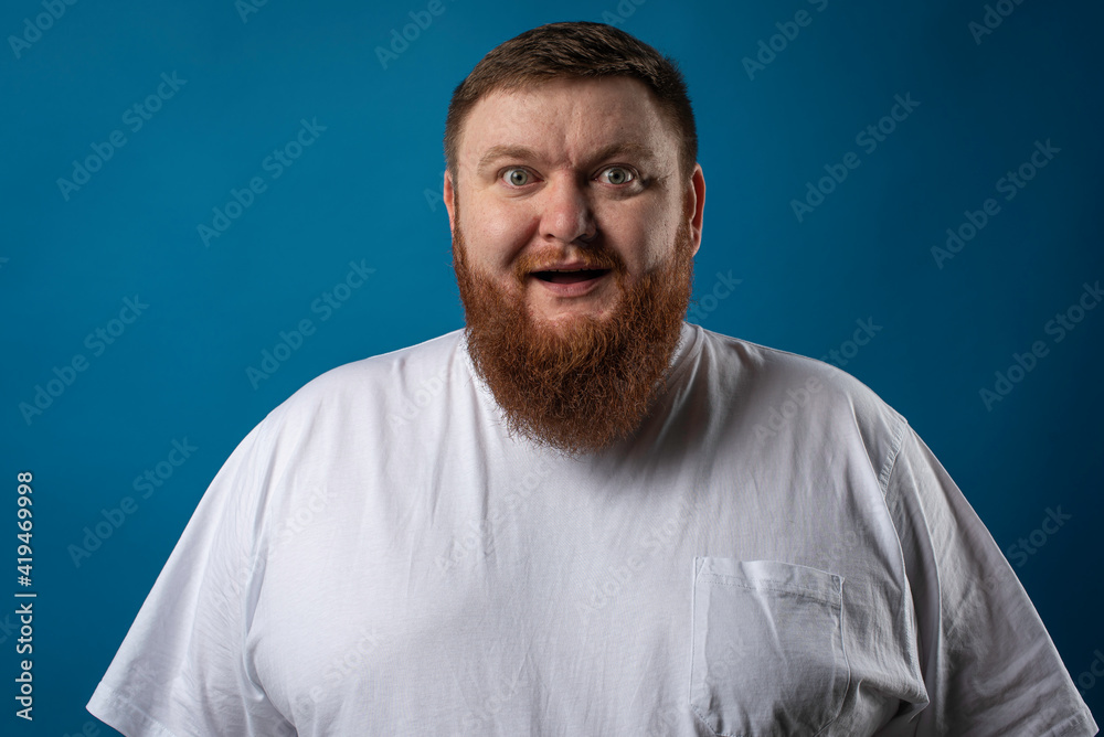Fototapeta premium portrait of a bearded cheerful, emotional and interesting man in a white T-shirt on a blue background, showing various hand gestures. Cheerful guy show business artist, host of a glamorous show. Body 