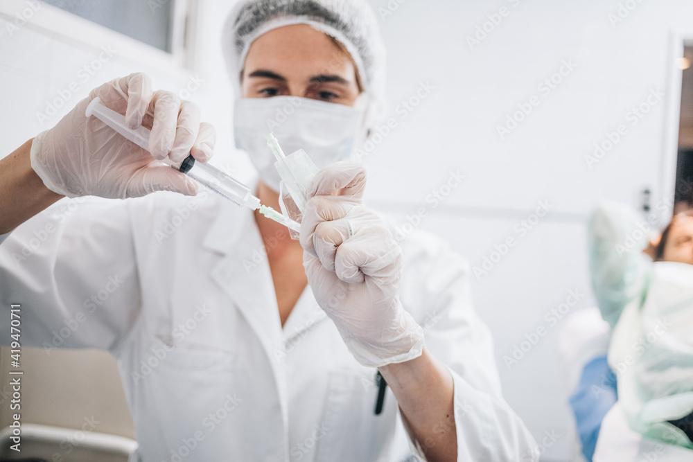 Doctor with mask, gloves and white cap covering a needle filled with anesthetic liquid in a hospital operating room
