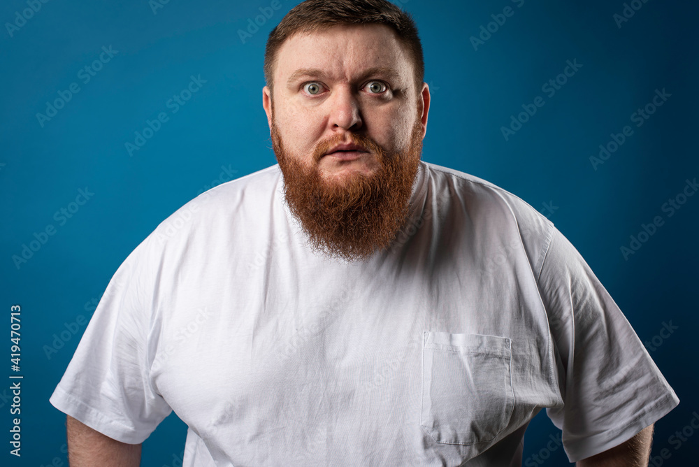 portrait of a bearded cheerful, emotional and interesting man in a white T-shirt on a blue background, showing various hand gestures. Cheerful guy show business artist, host of a glamorous show. Body portrait of a bearded cheerful, emotional and interesting man in a white T-shirt on a blue background, showing various hand gestures. Cheerful guy show business artist, host of a glamorous show. Body