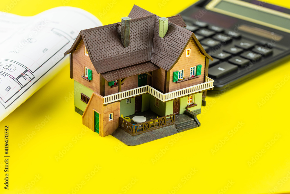 Buying a house or mortgage concept. Model toy house with calculator and plan on yellow background. Housing and Real Estate concept. Buying a house or mortgage concept. Model toy house with calculator and plan on yellow background. Housing and Real Estate concept.