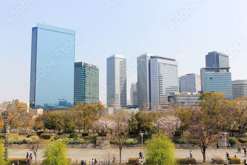 A cityscape of Osaka Business Park from Osaka Castle Park during cherry blossom season. Public park and high-rise buildings cityscape. Green environment city and downtown business district. photo