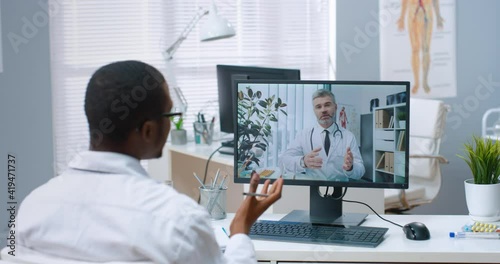 Wallpaper Mural Over shoulder view of African American male specialist talks on online video call with Caucasian middle-aged doctor on computer sitting in office experienced physician consults nurse on web conference Torontodigital.ca