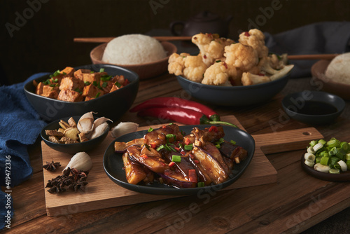 Mala tofu and yuxiang, chinese vegan dishes, accompanied by a bowl of rice, cauliflower, soy sauce and a Japanese teapot on top of a wooden table decorated with fabrics photo