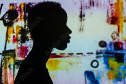 Silhouette of unrecognizable ethnic person standing against wall with projection of abstract painting photo