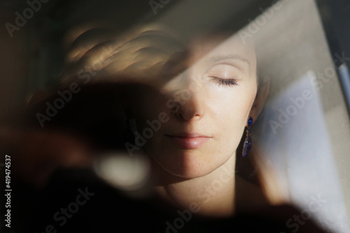 Through glass of peaceful adult lady with short hair recreating with closed eyes on sunny day photo