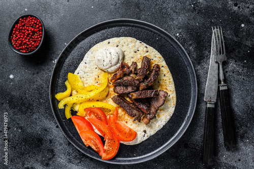 Tortilla with beef meat steak and fresh salad on a rustic plate. Black background. Top view