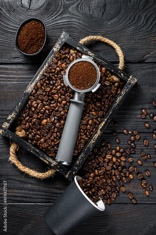 Ground Coffee in Portafilter for Espresso in a wooden tray with coffee beans. Black wooden background. Top view