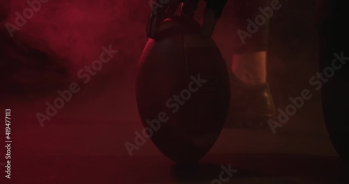 Crop rugby player with ball in dark studio. Unrecognizable male rugby player spinning ball in dark studio with red neon light and steam