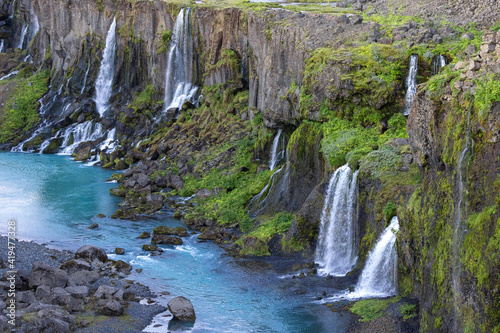 Spectacular view of rapid cascades flowing from rough rocky cliff covered with lush greenery into tranquil blue reservoir in peaceful nature