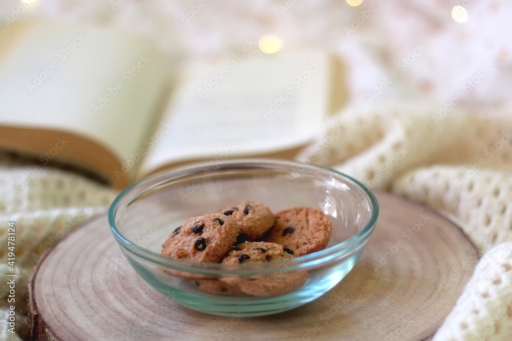 Bowl of chocolate chip cookies and open book on a bed. Selective focus. Bowl of chocolate chip cookies and open book on a bed. Selective focus.