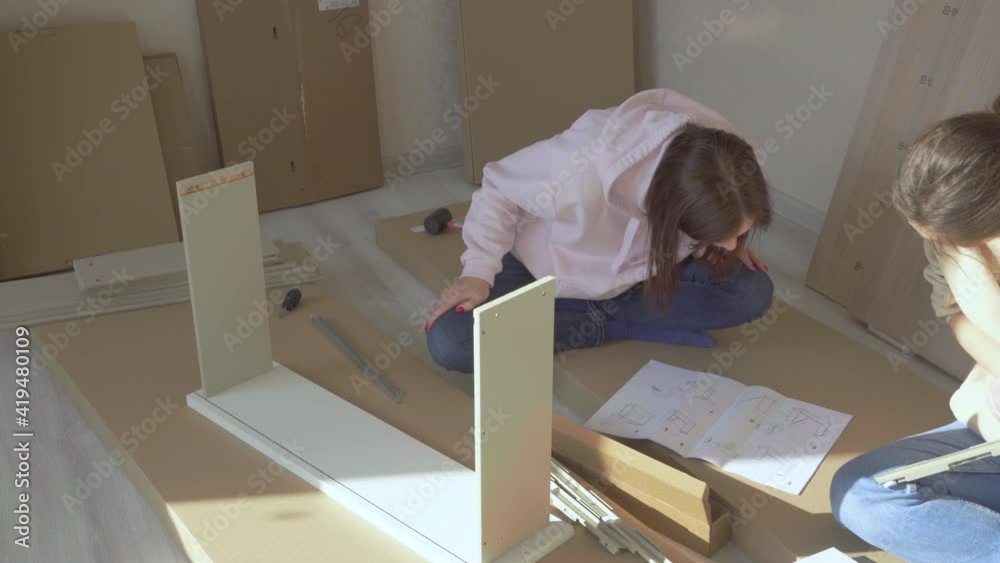 Women reading instructions to self assemble furniture in new home.