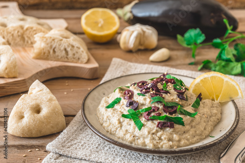 Arabian cuisine: Baba Ganoush with black olives and minced parsley and flatbread on a rustic wooden table