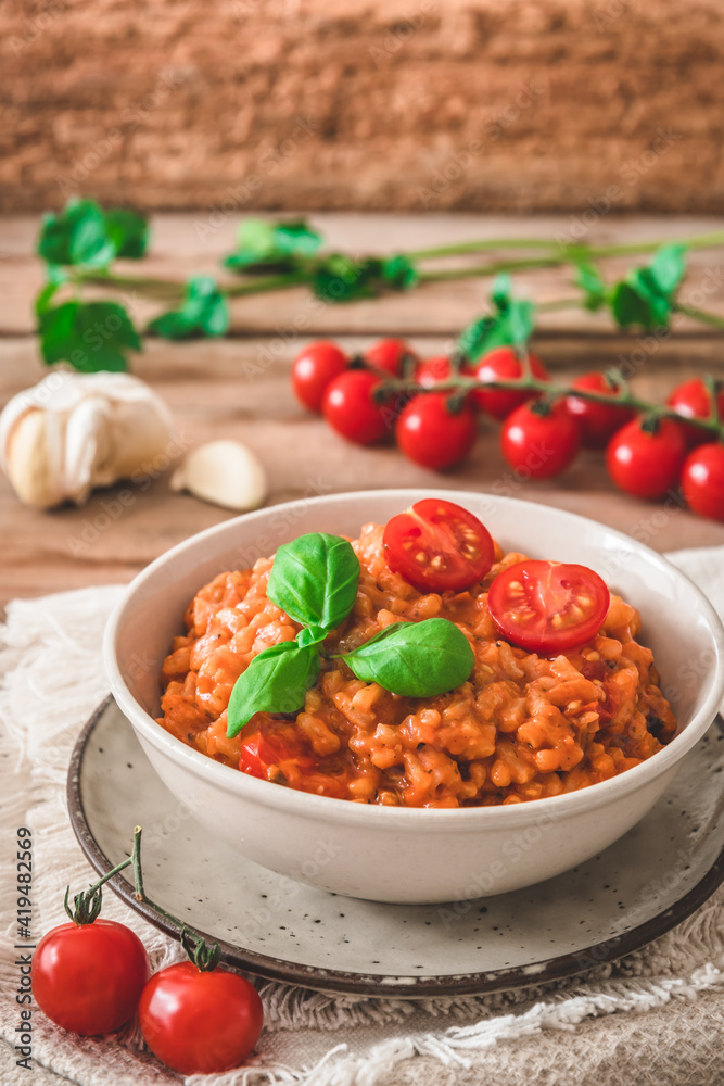 Homemade tomato risotto with fresh basil on a rustic wooden table, vertical Homemade tomato risotto with fresh basil on a rustic wooden table, vertical