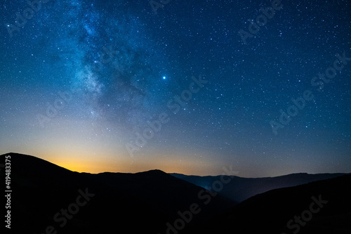 Picturesque view of starry blue sky with clouds over mount with mountains silhouettes at sunset