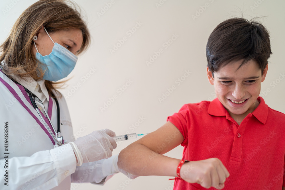 Female medic in mask making injection of vaccine from coronavirus for boy with grimace on face Female medic in mask making injection of vaccine from coronavirus for boy with grimace on face