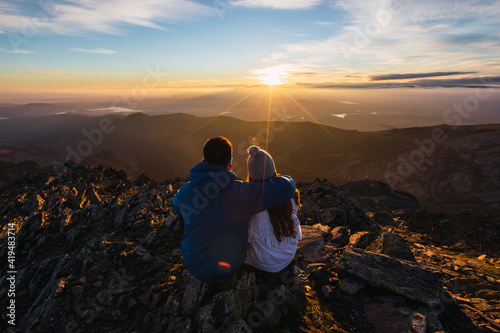 Back view of anonymous couple of tourists admiring majestic mountains under shiny sky in sunlight