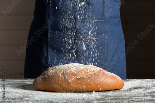 Crop anonymous baker sprinkling flour over fresh bread loaf placed on table while working in bakery photo