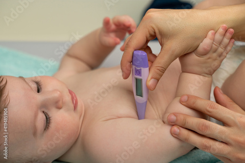 Crop loving mother measuring temperature of cute baby and placing thermometer in baby underarm carefully photo