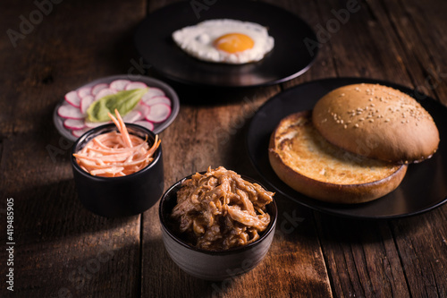 High angle set of ingredients for pulled pork hamburger with vegetables and fried egg arranged on wooden table