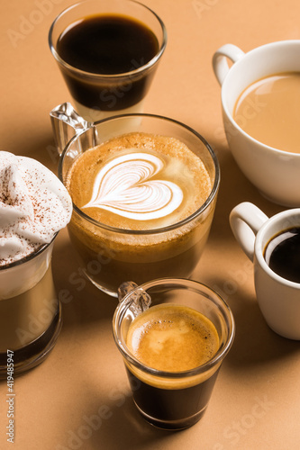Set of different classic kinds of aromatic coffee drinks served in cups of various sizes arranged on beige surface