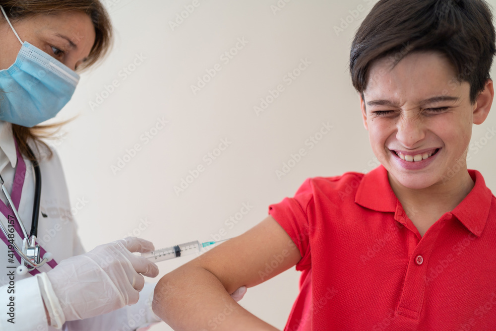 Female medic in mask making injection of vaccine from coronavirus for boy with closed eyes and grimace on face Female medic in mask making injection of vaccine from coronavirus for boy with closed eyes and grimace on face
