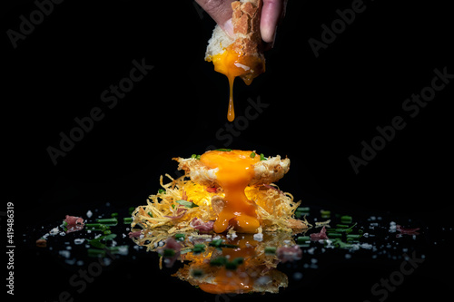 Appetizing crispy potato hash brown nest with egg yolk served on mirrored surface against black background