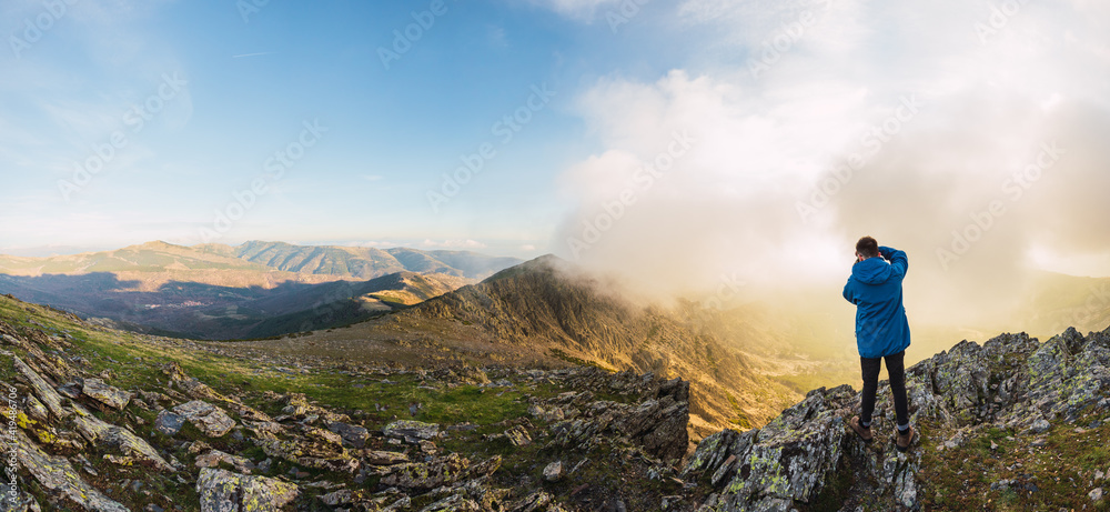 From above back view of anonymous male traveler with backpack taking photo of mount on camera on foggy day From above back view of anonymous male traveler with backpack taking photo of mount on camera on foggy day