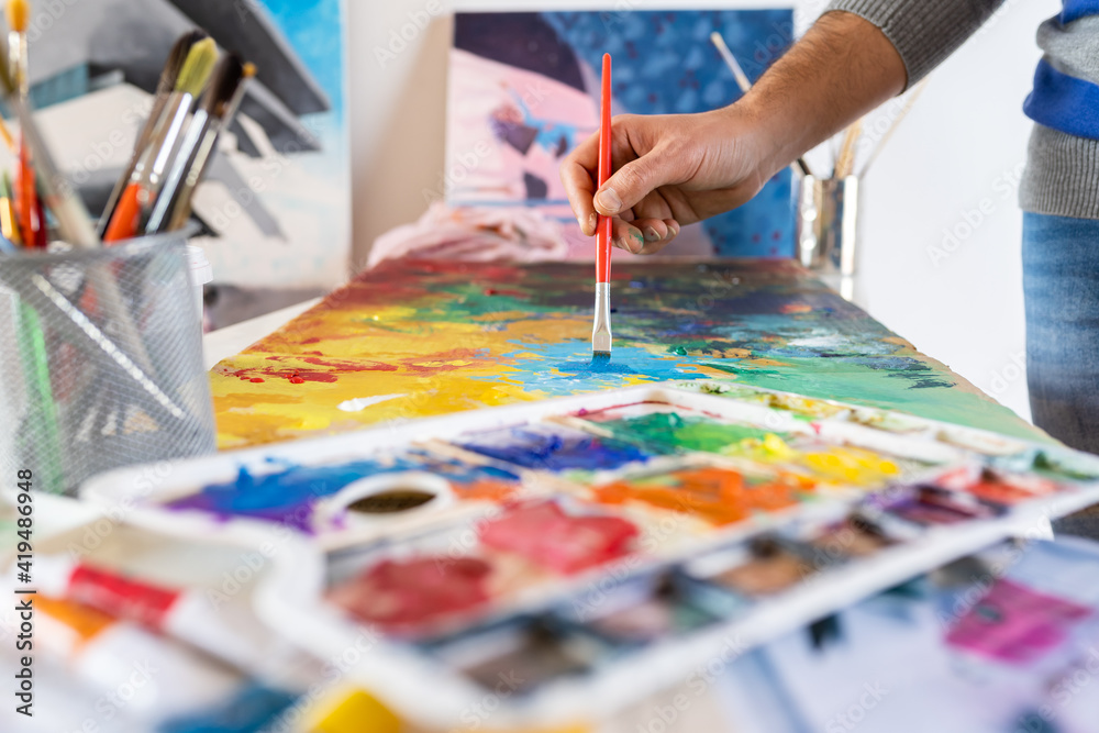 Crop unrecognizable male painter using professional brush during painting process on carton sheet near art tools in workroom Crop unrecognizable male painter using professional brush during painting process on carton sheet near art tools in workroom