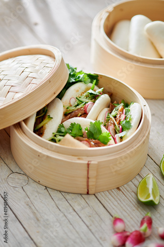 From above of tasty steamed baozi buns with radish and cucumber slices with meat and fresh cilantro on table photo