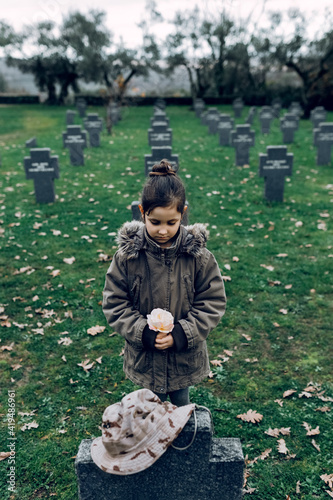 High angle of small kid mourning death of soldier fighting in war at graveyard