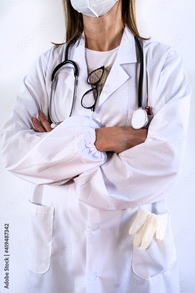 Cropped unrecognizable female doctor in white uniform and stethoscope wearing protective medical mask standing with arms crossed Cropped unrecognizable female doctor in white uniform and stethoscope wearing protective medical mask standing with arms crossed
