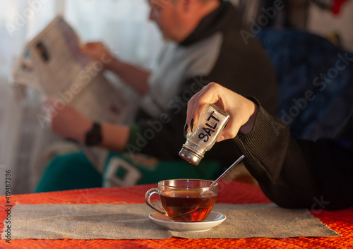 APRIL'S JOKE: Girl pours salt into tea while father reads newspaper	