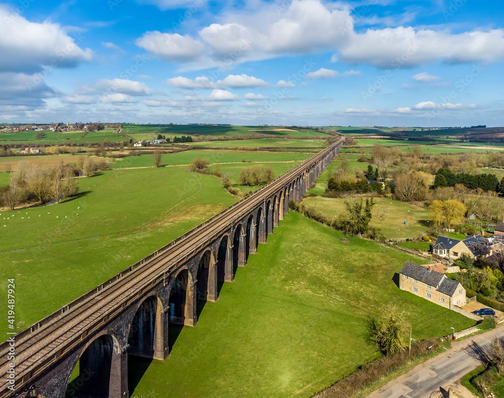 An aerial view of the sun illuminating the spectacular Harringworth railway viaduct as it crosses the Welland Valley on a sunny day in the UK