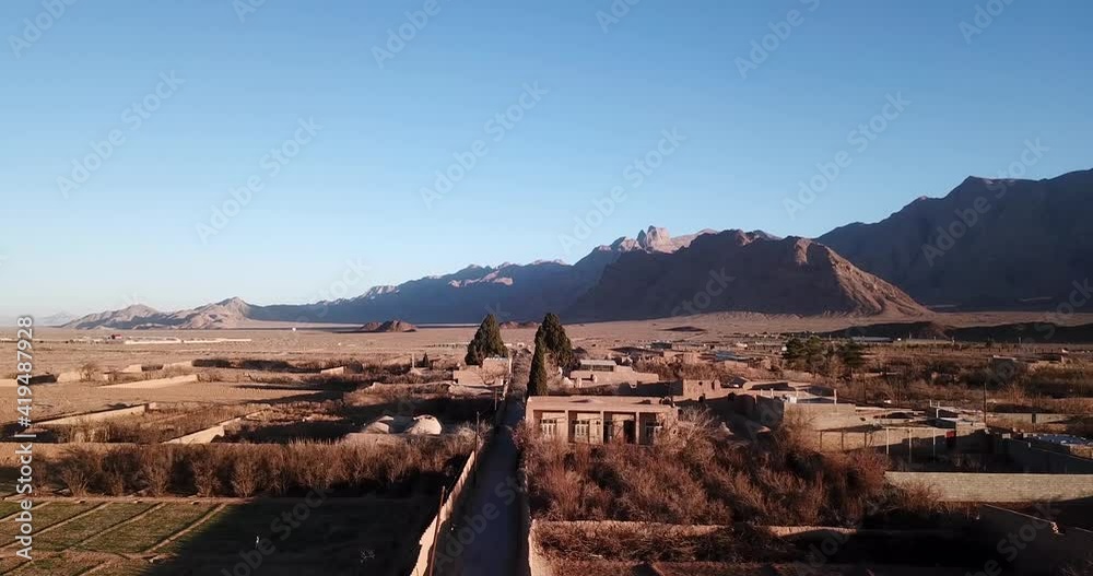Twin Holy Old Cypresses Trees in an Ancient Village of Zoroastrian People Mobarakeh in Yazd Iran in The Middle of Dessert with Landscape of Transit Road TIR and Mountains in Background in Sunset Time