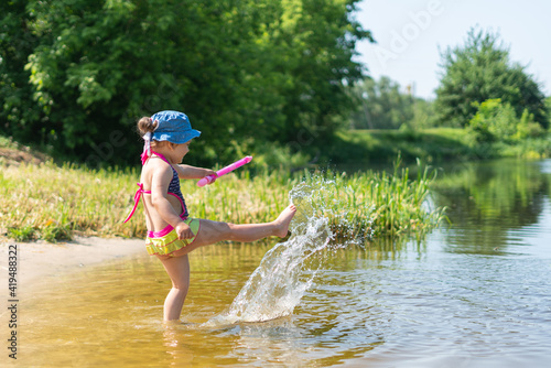 Fototapeta Naklejka Na Ścianę i Meble -  Happy little girl swimming and splashing in the lake on a hot sunny day
