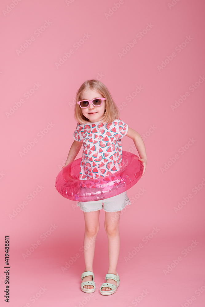 girl in sunglasses and an inflatable water circle on a pink background