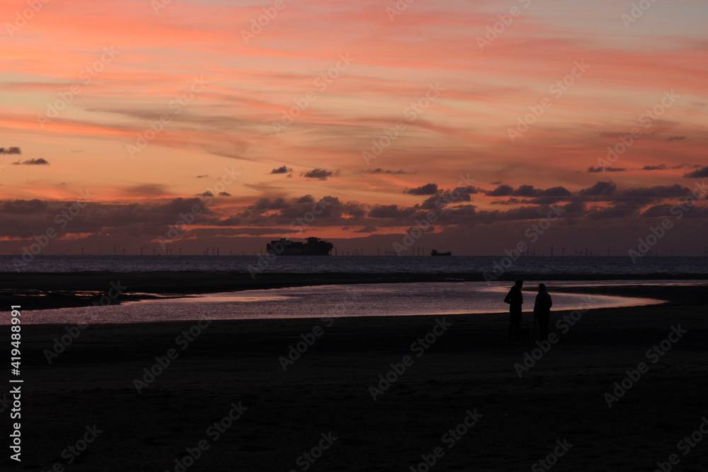 silhouettes of couple and boats on sunset beach Cadzand