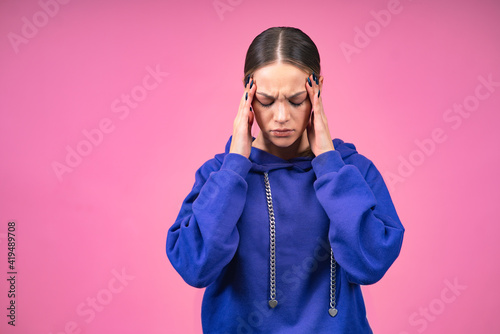 pink isolated background. Sick girl, a young tense, tired nervous woman suffering from pain, headache, migraine, holding her sore head temples with her hands. Feeling unwell, feeling unwell, pain. © Дарья Шуйскова